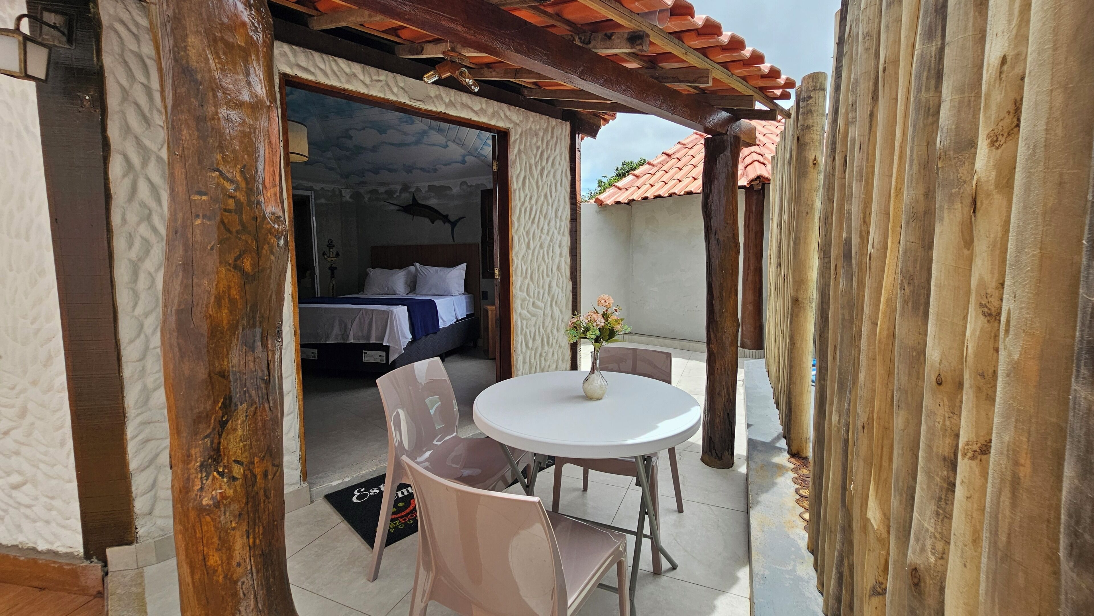 A room with a bed, a small table with a vase, and a chair.