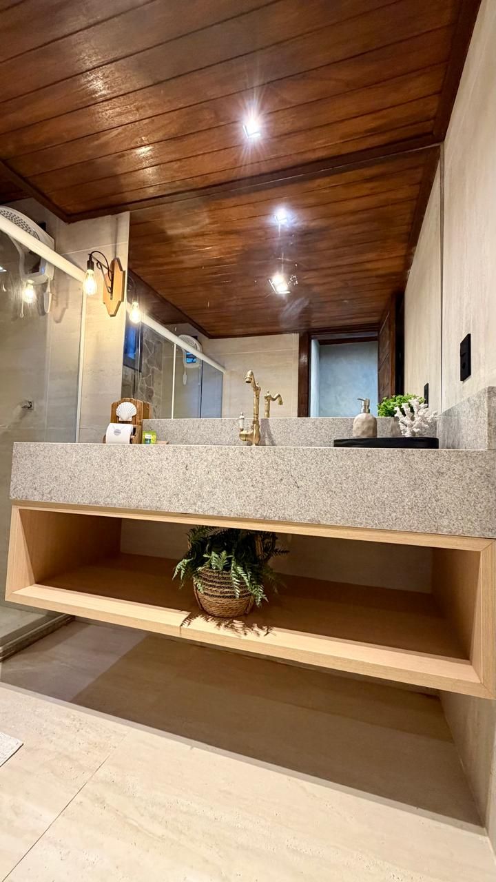 A bathroom with a wooden ceiling, a granite countertop, a sink with a gold faucet, and a mirror.