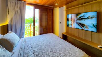 Quarto com cama, televisão fixada na parede e porta de vidro deslizante para uma varanda.