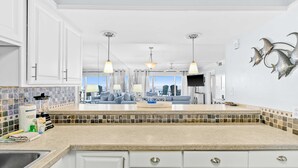 A modern kitchen with white cabinets, a tiled backsplash, and pendant lighting. - Snowbird-friendly Gulf-front condo with outdoor pool & gym (Miramar Beach)