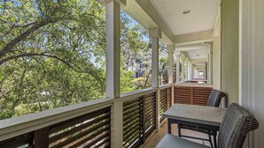 A covered outdoor balcony with a table and chairs, surrounded by trees. - Coastal Chic Retreat | Pools | Tennis Court| Private Beach Access (Santa Rosa Beach)