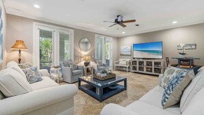 A spacious living room with a ceiling fan, a large flat-screen TV, and a comfortable seating area with sofas and a coffee table. - Coastal Chic Retreat | Pools | Tennis Court| Private Beach Access (Santa Rosa Beach)
