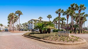 A paved area with a sign reading "Gulfplace," surrounded by palm trees and a building in the background. - Coastal Chic Retreat | Pools | Tennis Court| Private Beach Access (Santa Rosa Beach)