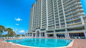 A large hotel with a swimming pool, multiple balconies, and a clear blue sky. - Family-friendly beach condo with coastline views, balcony, shared pool, gym, tennis (Miramar Beach)