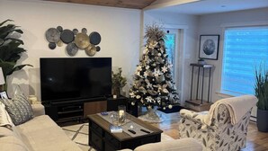 A modern living room with a large flat-screen TV, a Christmas tree, and a cozy seating area. - Waterfront Sunset Cove (Goobies)