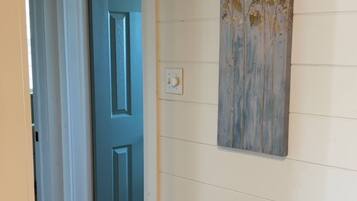 A hallway with a blue door, a light switch, and a wall-mounted artwork of flowers.
