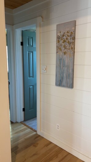 Un pasillo con una puerta azul, un interruptor de luz y una obra de arte floral en la pared.