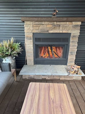 A stone fireplace with a fire, a wooden bench, and a potted plant.