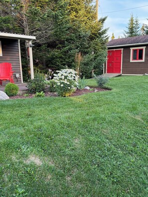 Un césped bien cuidado con una pequeña zona de jardín con flores blancas y una silla roja.