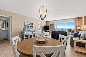 A modern living room with a dining area, a TV, and a view of the ocean. - Ground floor oceanfront beachy condo with furnished patio, outdoor pool, gym (Miramar Beach)
