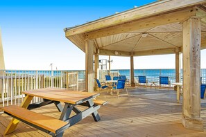 Eine Holzterrasse mit Picknicktischen und -stühlen mit Blick auf einen Strand.