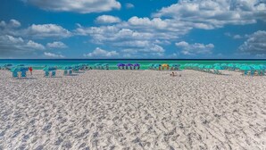 Una playa con filas de sombrillas y sillas de descanso, un cielo despejado y el océano al fondo.