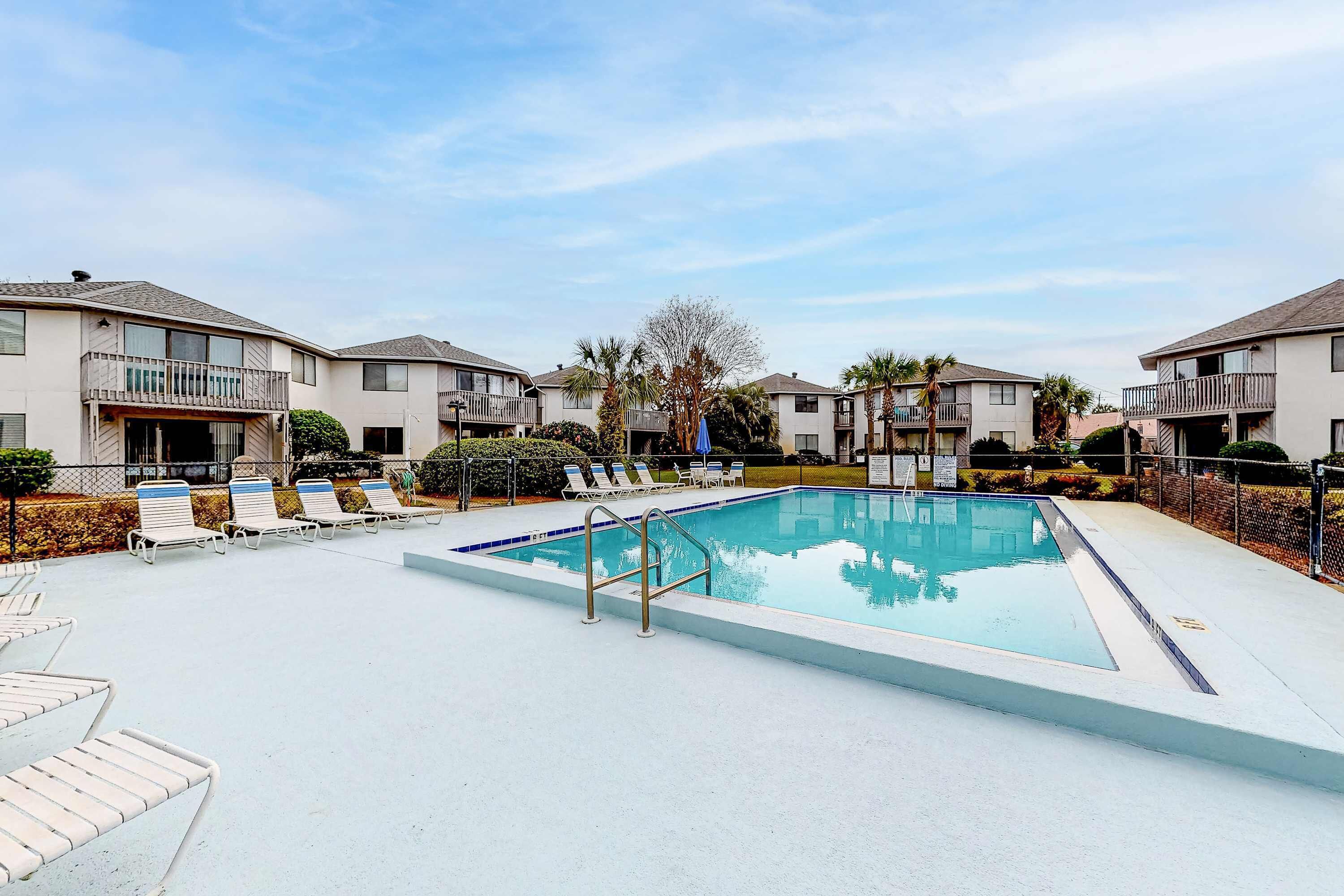 A swimming pool with lounge chairs and a fence, surrounded by apartment buildings.