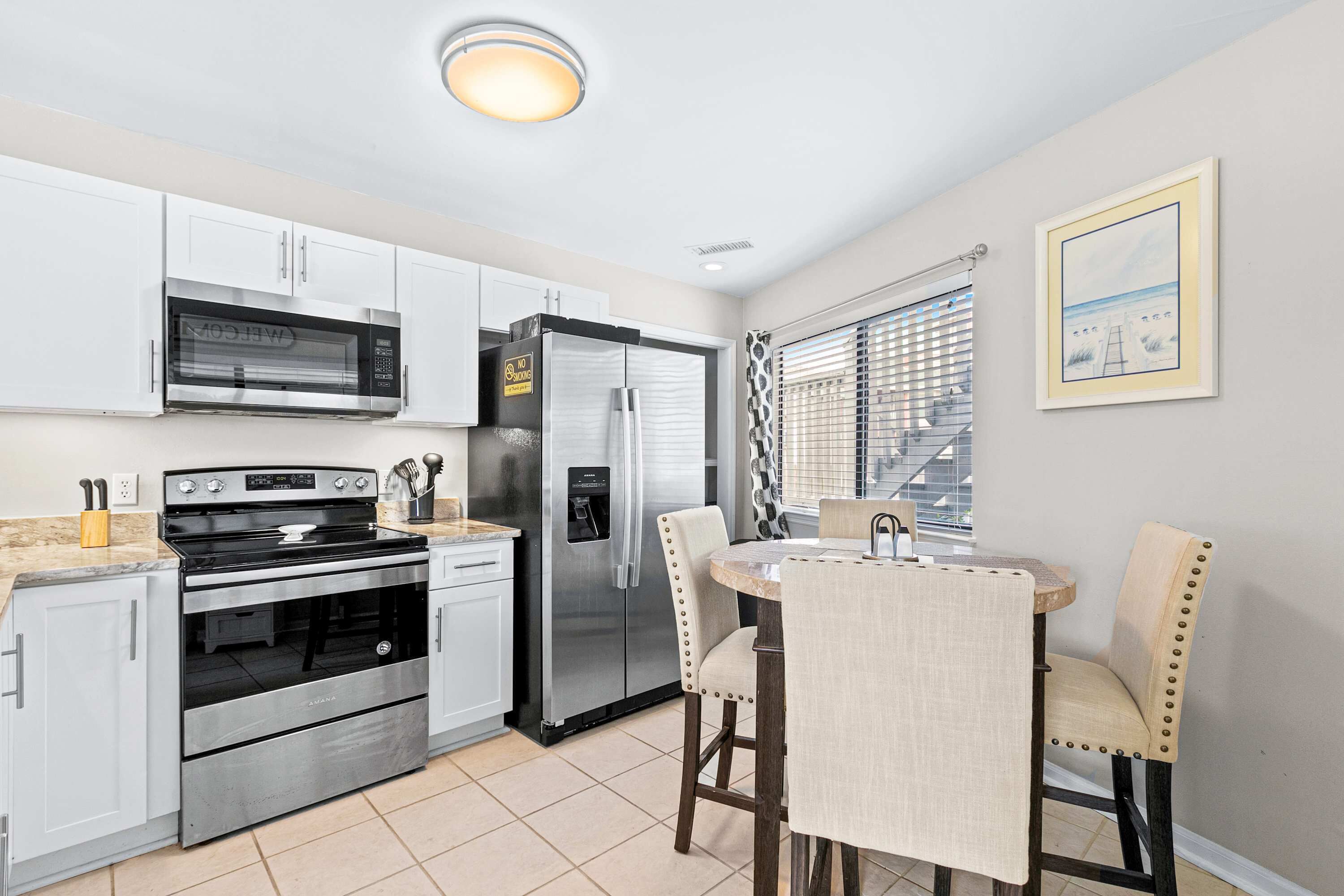 A modern kitchen with white cabinets, stainless steel appliances, and a dining area with two chairs and a table.