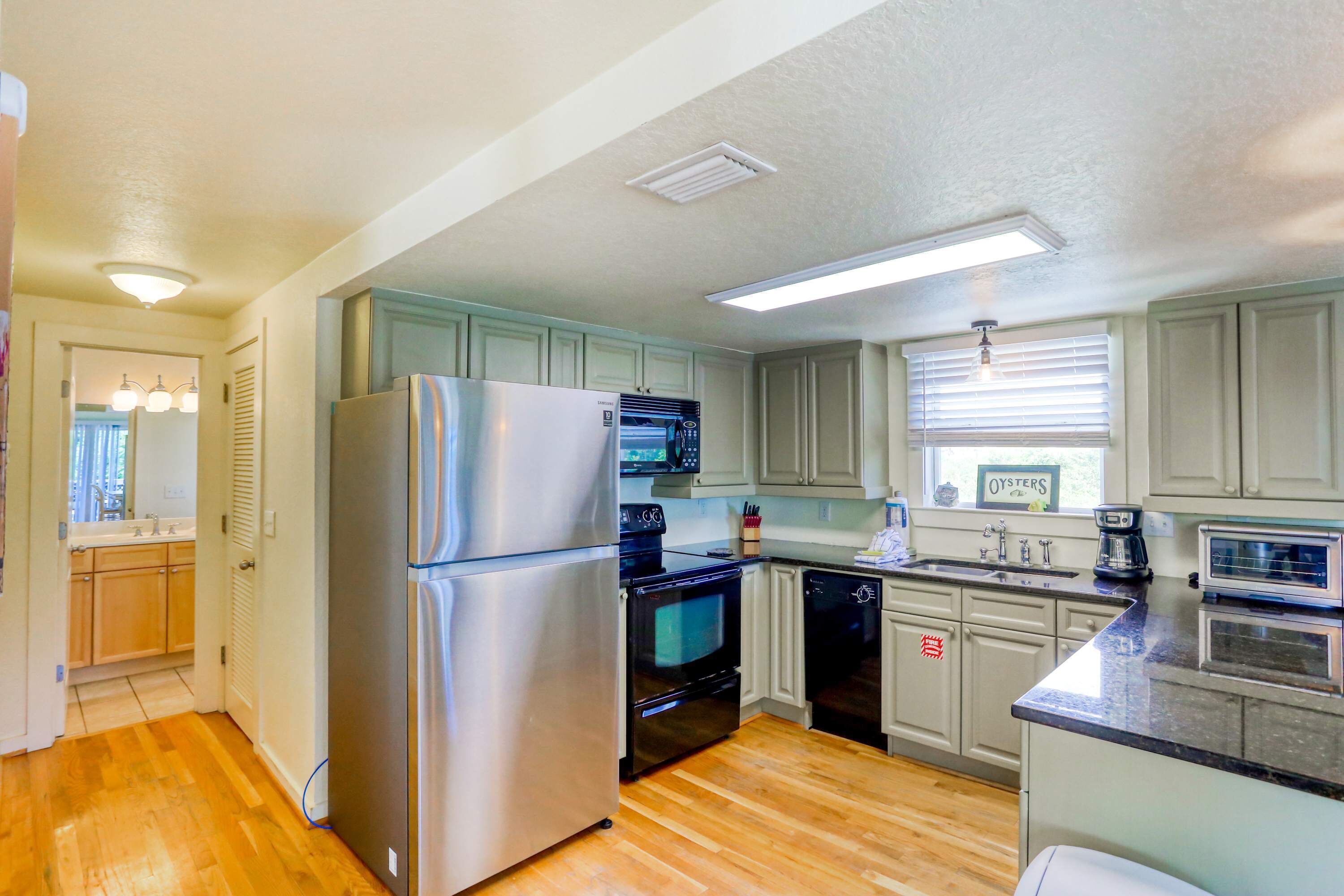 A modern kitchen with stainless steel appliances, wooden flooring, and light-colored cabinets.