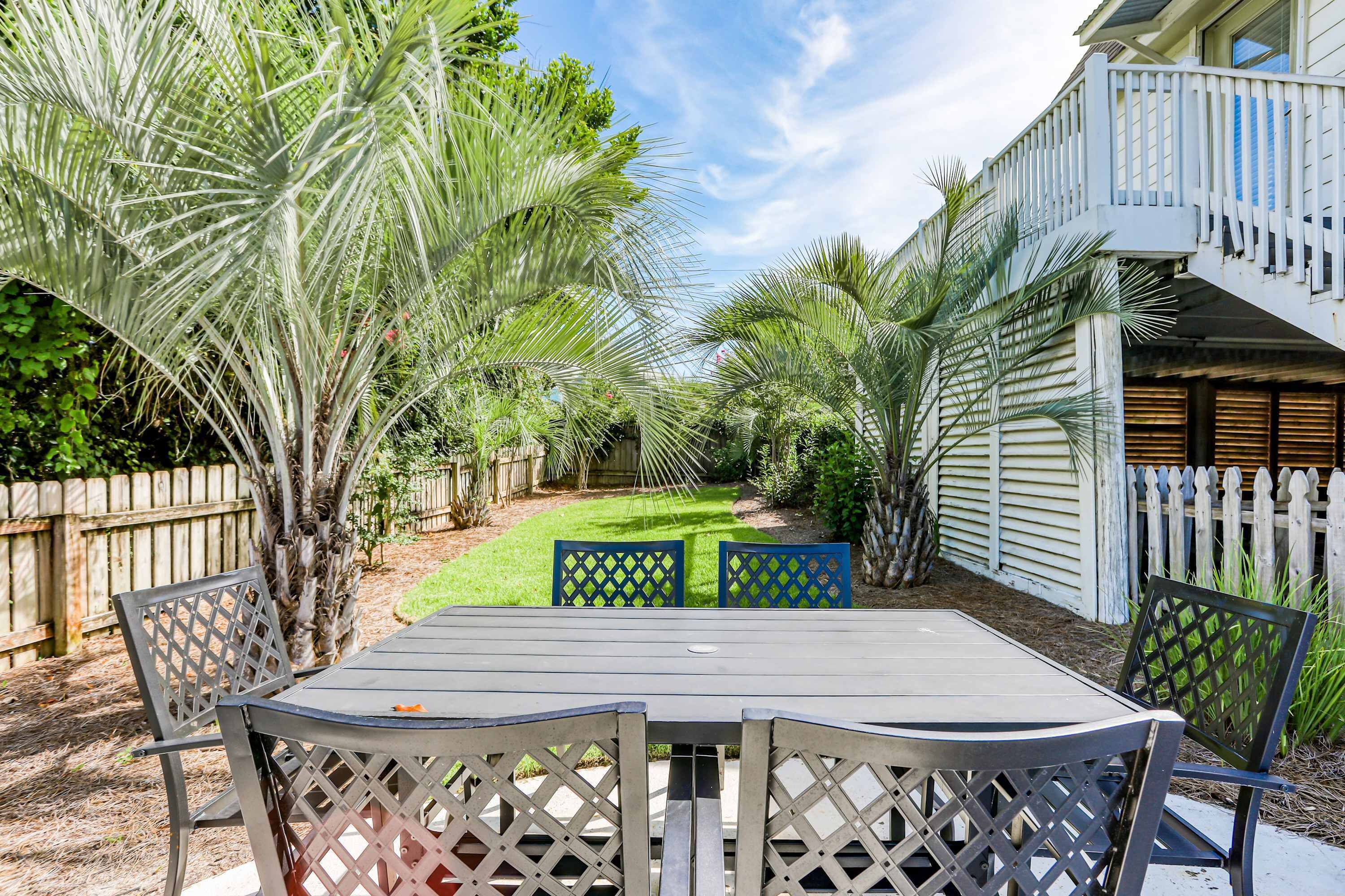 A patio with a table and chairs, surrounded by a wooden fence and palm trees.