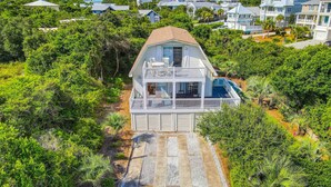 A two-story house with a balcony, surrounded by dense greenery and a clear sky. - Dog-friendly, Gulf-view home with pool, decks, WiFi, & WD - walk to beach (Santa Rosa Beach)