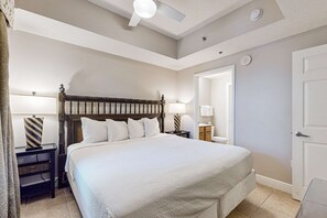 A neatly arranged bedroom with a large bed, bedside tables, a ceiling fan, and a door leading to another room. - Gulf View Condo in Miramar Beach with Pool ,Gym and Beach Access (Miramar Beach)