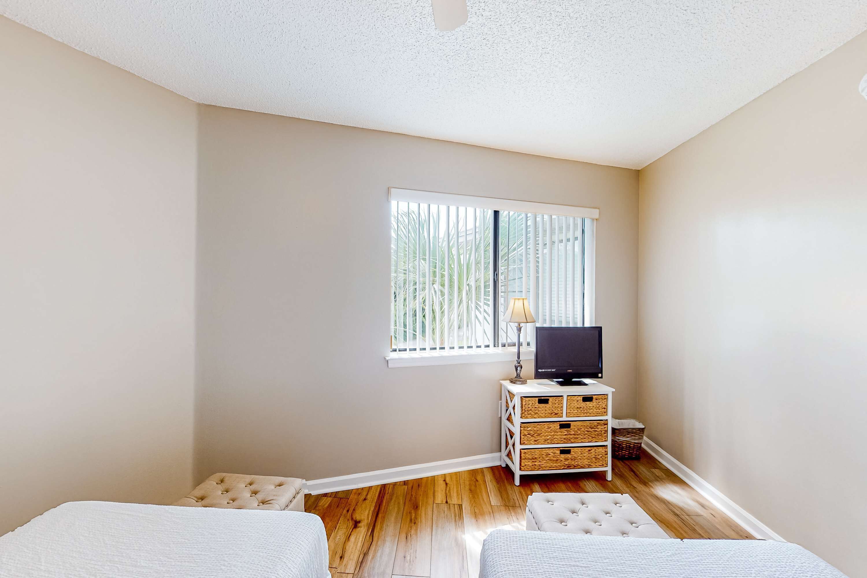 A bedroom with a bed, a TV, a window with blinds, and a small white dresser.