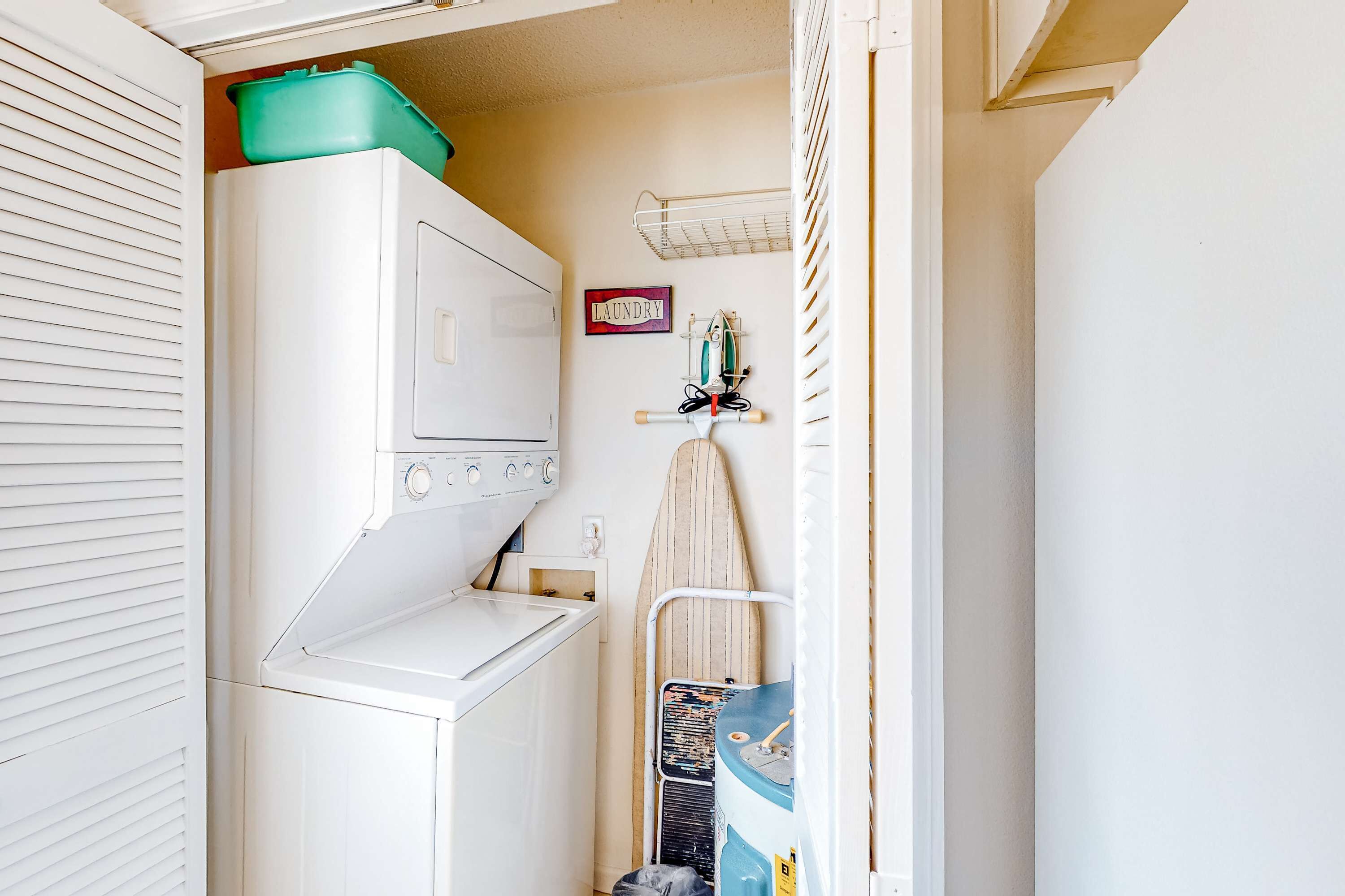 A compact laundry area with a washing machine, a drying rack, and a small ironing board.