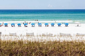 Ein Strand mit weißem Sand, blauen Sonnenschirmen und einigen Liegestühlen.