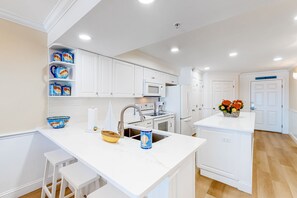A modern kitchen with white cabinetry, a central island with stools, a microwave, and a sink. - Second floor oceanfront condo w ocean view, washer&dryer, AC, and pool access (Fort Walton Beach)