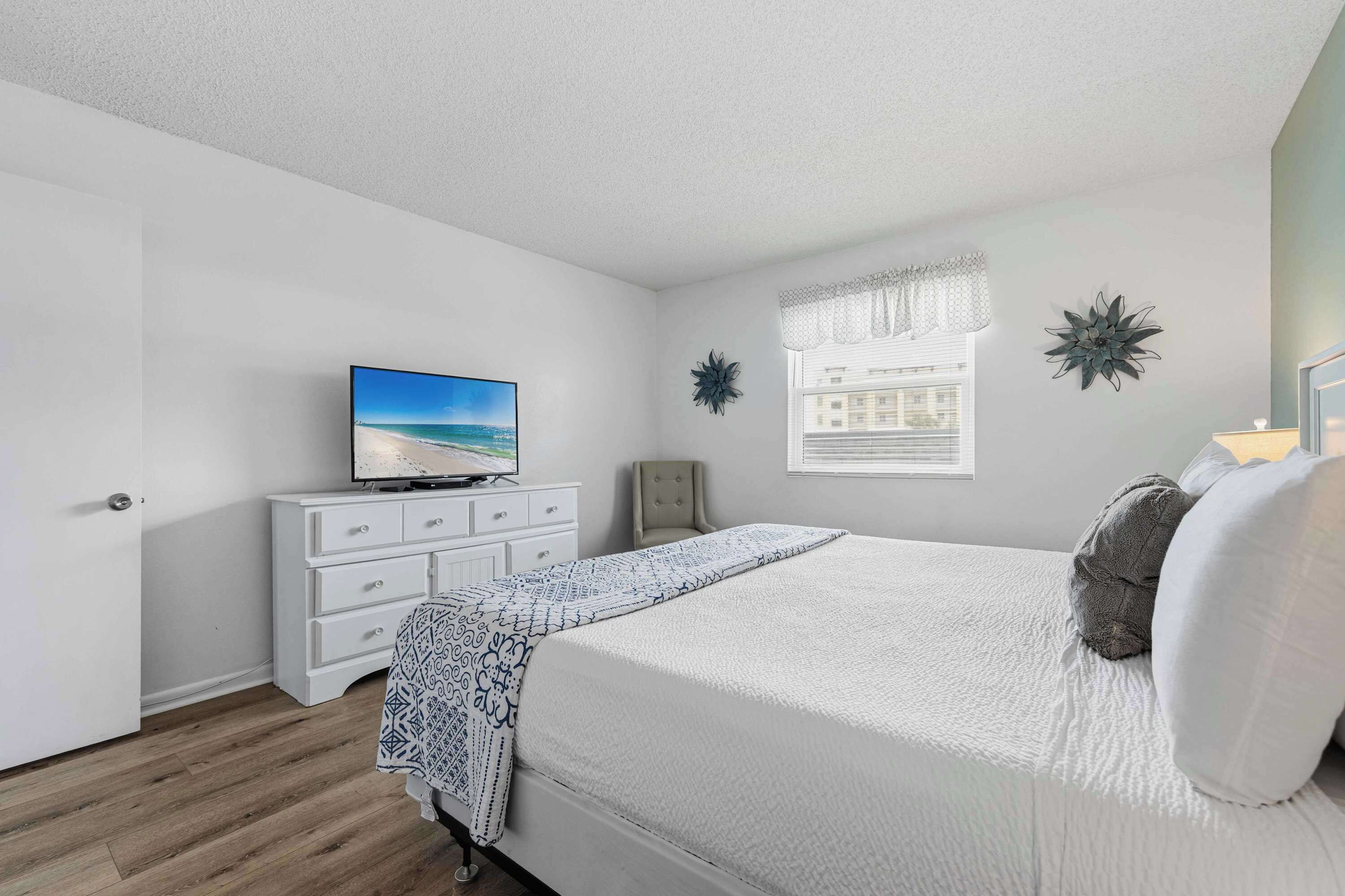 A bedroom with a bed, a television on a dresser, a window with a view, and decorative wall art.