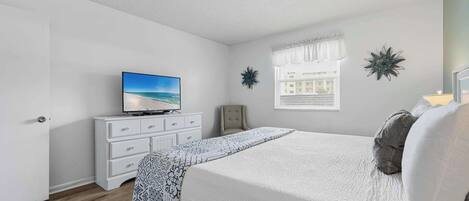 A bedroom with a bed, a television on a dresser, a window with a view, and decorative wall art.