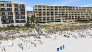 A beachfront hotel with multiple balconies, a sandy beach, and a boardwalk leading to the water. - Cozy coastal condo with shared pool, wifi and beach access (Fort Walton Beach)
