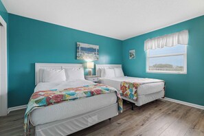 A bedroom with teal walls, two beds, a window with blinds, and a painting above the window. - Cozy coastal condo with shared pool, wifi and beach access (Fort Walton Beach)