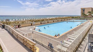 Una piscina con cubierta de madera, vista a la playa y un edificio al fondo.