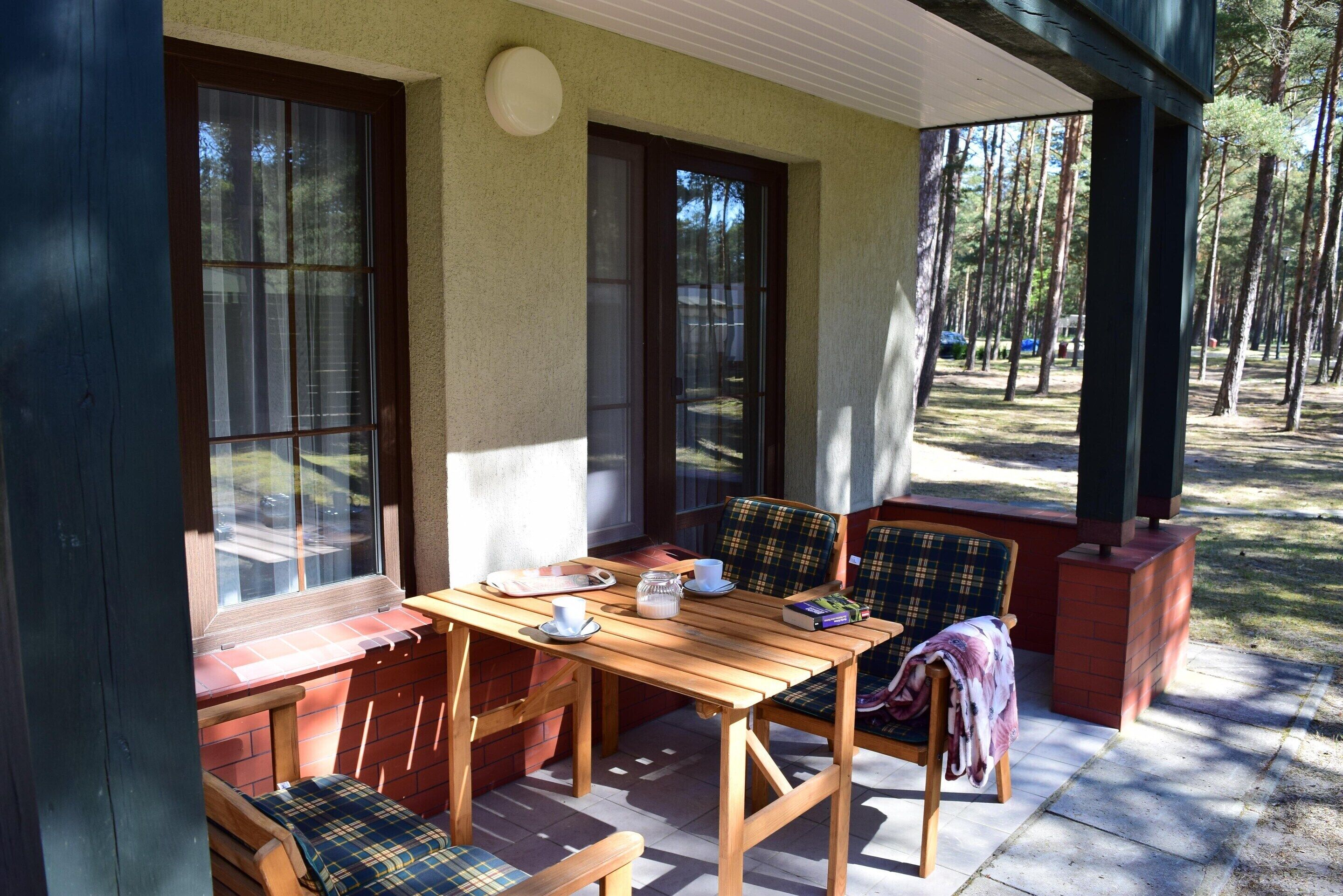 A covered patio with a wooden table and chairs, a brick fireplace, and large windows.