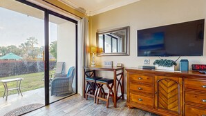A room with a sliding glass door leading to a patio, a television mounted on the wall, a wooden cabinet with drawers, and a small table with two chairs. - Comfy studio suite with pool & picnic area - snowbird-friendly (Fort Walton Beach)