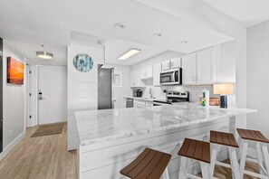 A modern kitchen with white cabinetry, a marble island, and bar stools. - Sunny, beachfront condo with shared pool, free WiFi, & Gulf views (Fort Walton Beach)