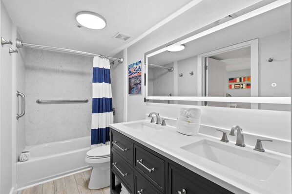 A modern bathroom with a bathtub, toilet, and vanity with a large mirror. - Sunny, beachfront condo with shared pool, free WiFi, & Gulf views (Fort Walton Beach)