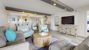 Un salón amplio con una televisión de pantalla plana grande, una mesa de centro de madera y un sofá con un cojín azul.