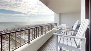 Un balcón con vista a la playa, sillas blancas y una terraza de madera.