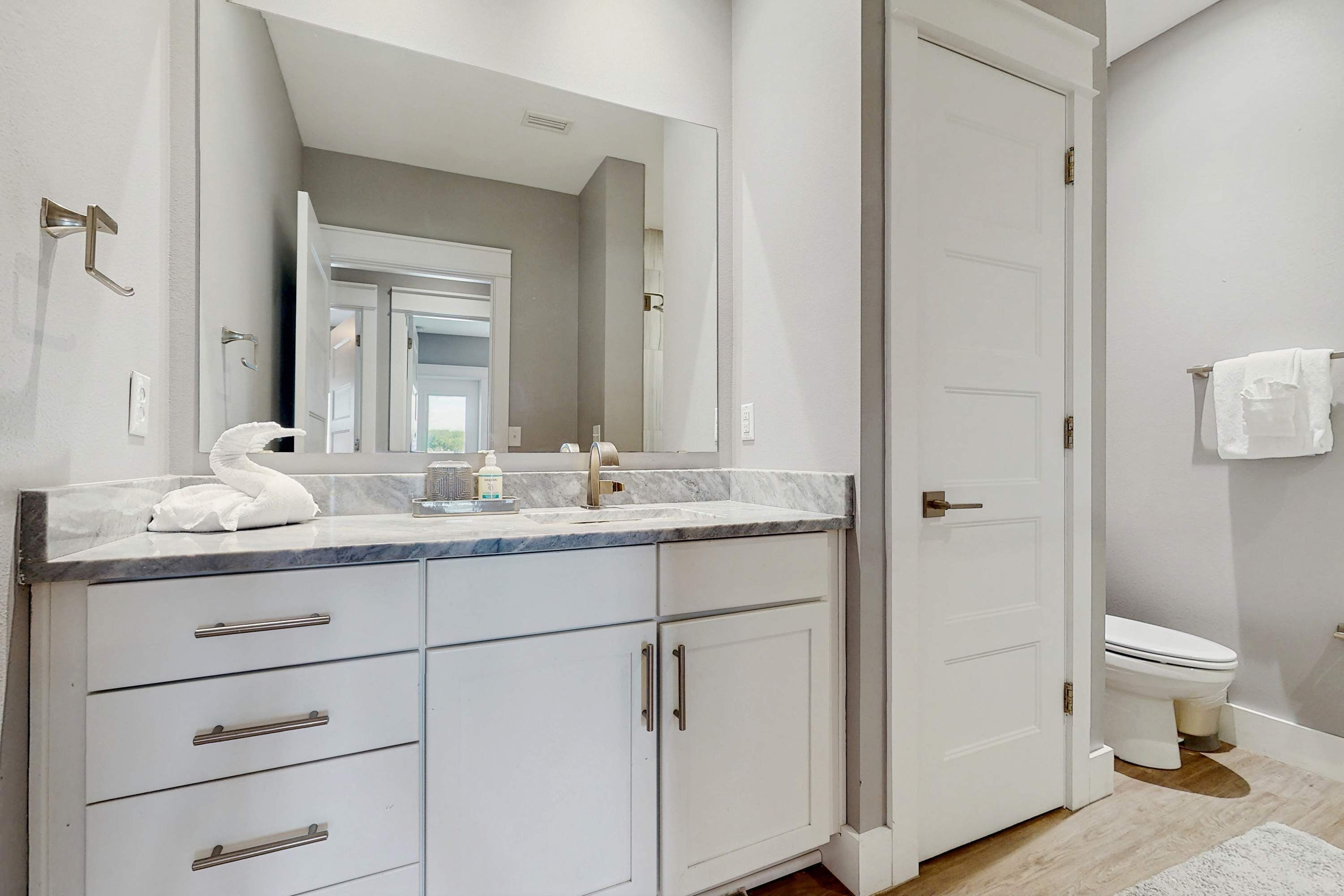 Une salle de bain avec un meuble-lavabo blanc, un grand miroir, des toilettes et un porte-serviettes.