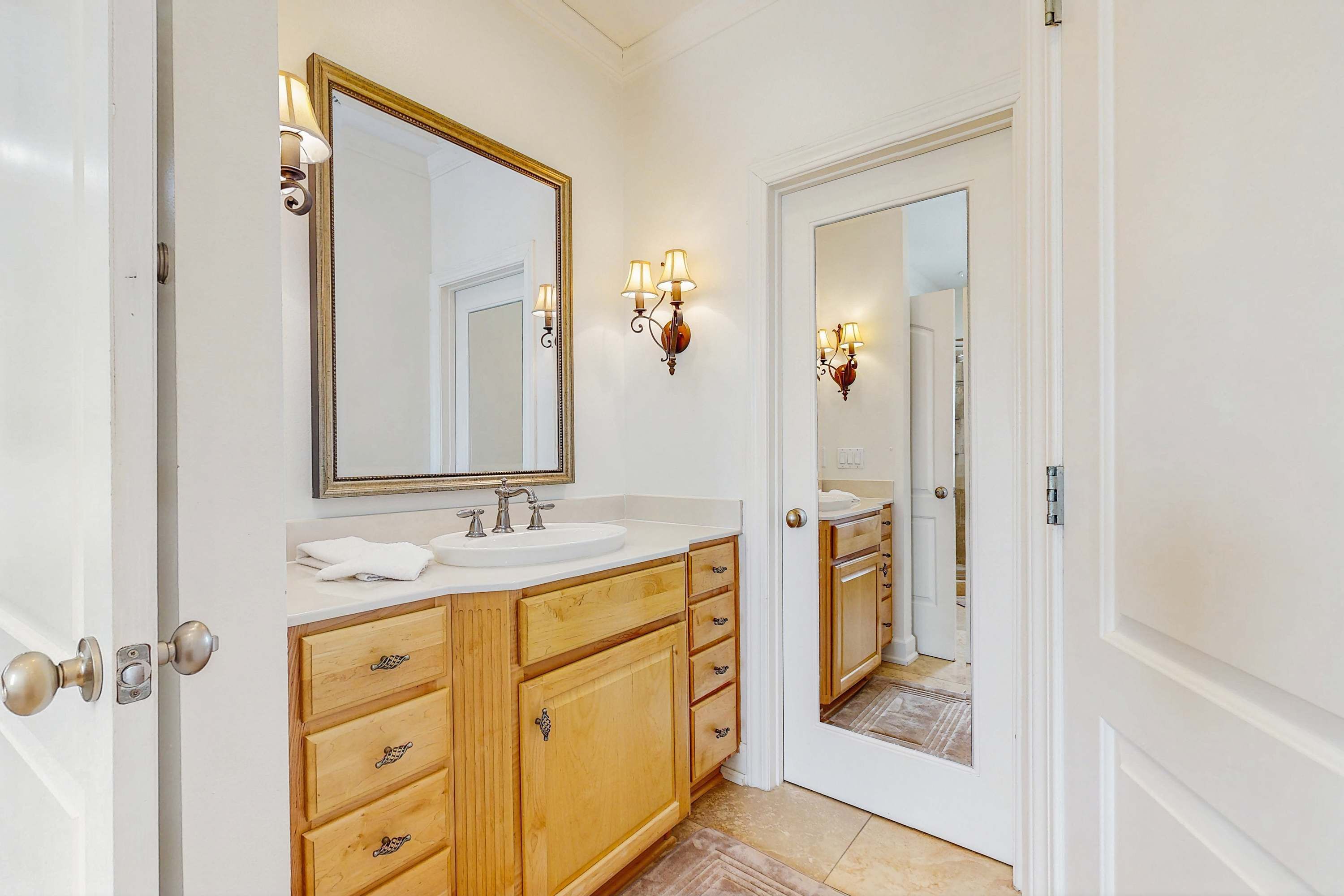A bathroom with a double sink vanity, wooden cabinetry, a large mirror, and wall sconces.