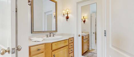 A bathroom with a double sink vanity, wooden cabinetry, a large mirror, and wall sconces.