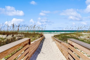 Ein hölzerner Weg führt zu einem Strand mit blauem Himmel und Meerblick.