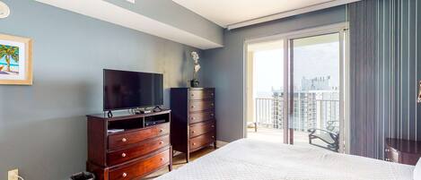 A bedroom with a large bed, a dresser, a television, and a balcony with a city view.