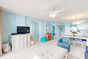 A spacious living area with a television, white cabinets, a dining table, and a ceiling fan. - Fourth floor spacious, beachfront condo with views - close to entertainment (Fort Walton Beach)