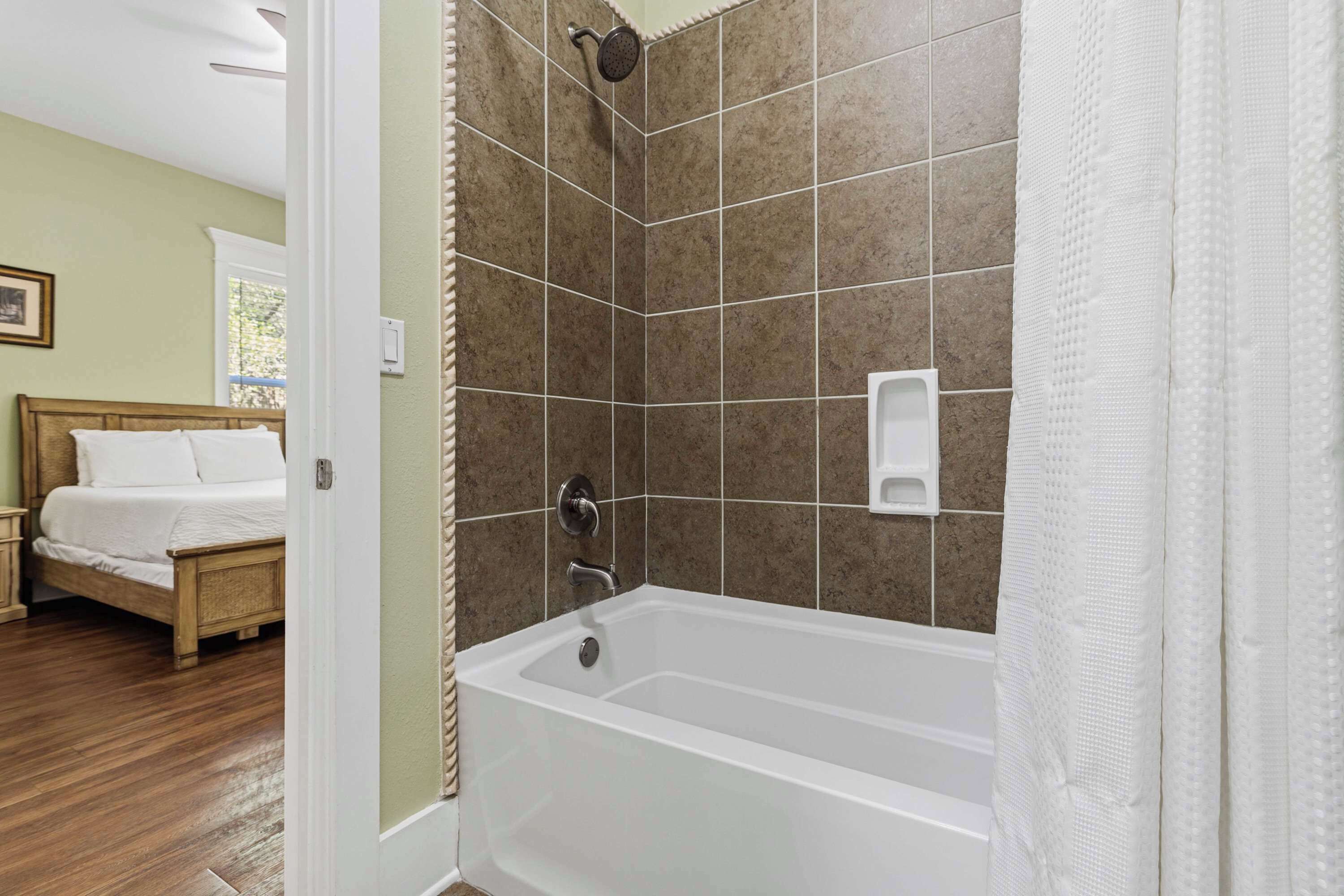 A bedroom with a wooden bed, a white bathroom with a bathtub, and a shower.