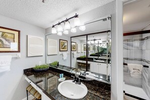 Ein modernes Badezimmer mit einem großen Spiegel, einem weißen Waschbecken und einer Duschkabine aus Glas.