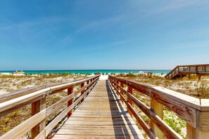 Ein Holzsteg führt zu einem Strand bei blauem Himmel.
