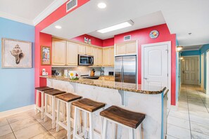 A kitchen with a central island, wooden bar stools, a microwave, a refrigerator, and a microwave above the island. - Cute 3BR Oceanfront 2nd-Floor | Balcony | Pool (Fort Walton Beach)