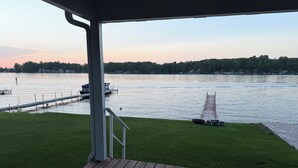 Une terrasse en bois dotée d’une rambarde, surplombant une étendue d’eau calme, avec un quai et un voilier.