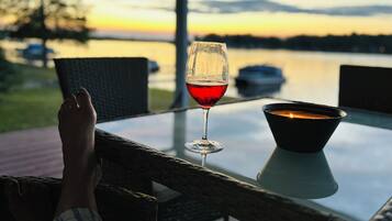 A glass of red wine on a table with a candle, overlooking a body of water and a sunset.