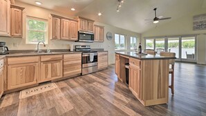 Une cuisine spacieuse avec des meubles en bois, un grand îlot central, des appareils électroménagers en acier inoxydable et une vue sur l’extérieur.